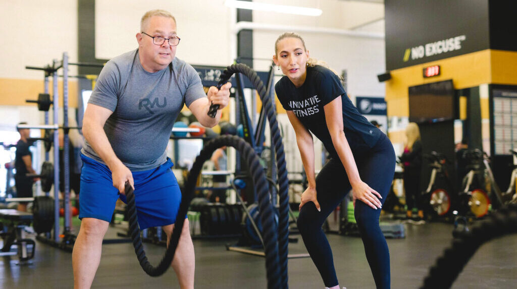 En man och en kvinna tränar tillsammans med stridslinor på ett gym, med fokus på styrketräning.