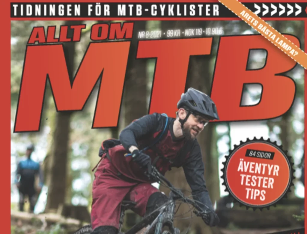 En mountainbikecyklist i svart och röd outfit åker på en skogsstig. Tidningens omslag har stor röd "MTB"-text och främjar innehåll om äventyr, tester och tips.