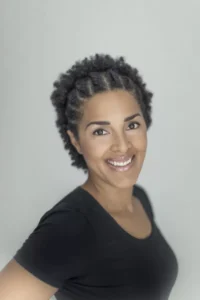 En leende person med kort lockigt hår och klädd i en svart skjorta poserar mot en vanlig ljus bakgrund. - Aktivitus En leende person med kort lockigt hår och klädd i en svart skjorta poserar mot en vanlig ljus bakgrund.