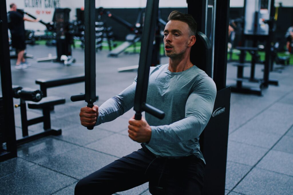 En man på ett gym fokuserar på att använda en bröstpressmaskin medan han bär en långärmad skjorta och byxor.
