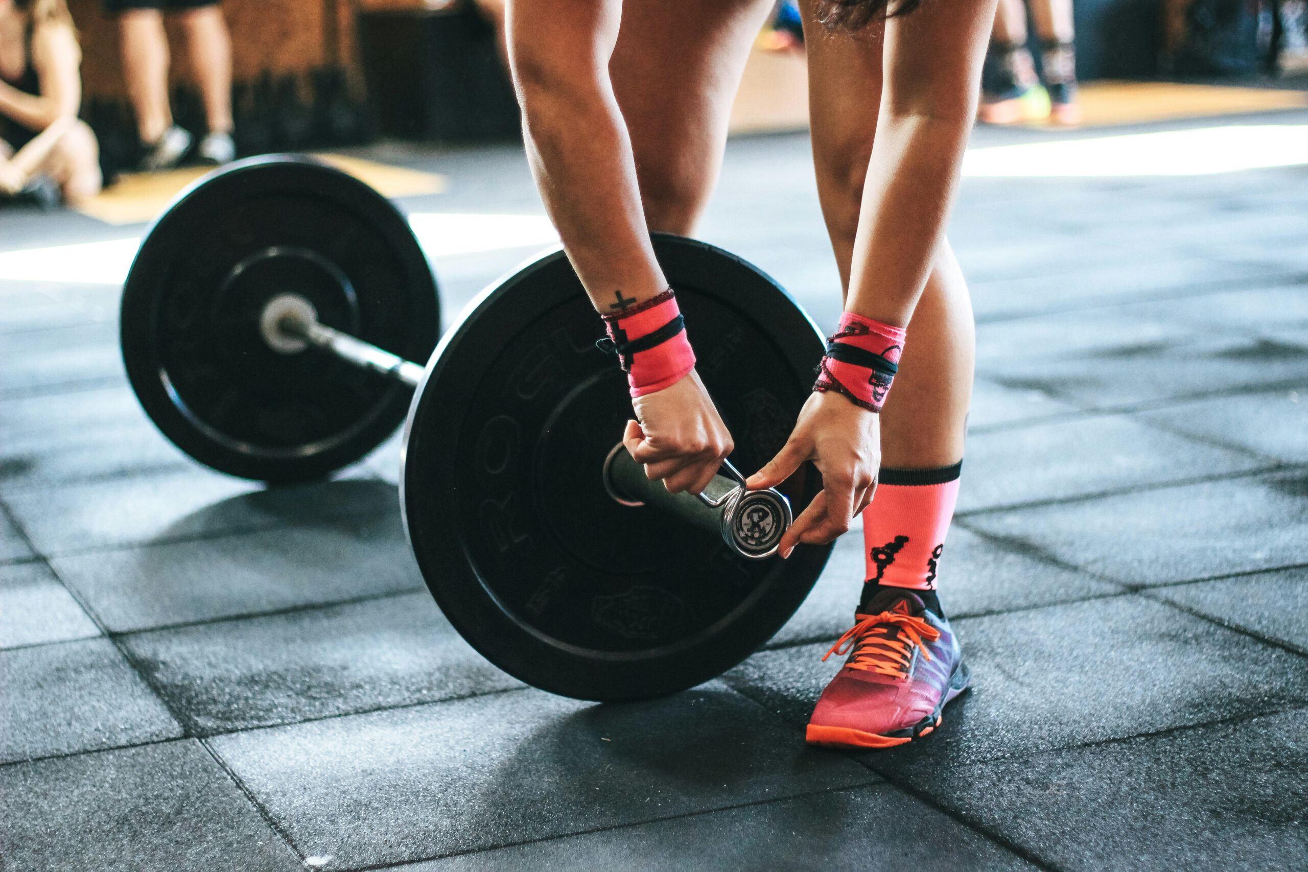 Person som drar åt vikter på en skivstång på gymmet, bär ljust rosa strumpor och skor med ett svart gummigolv i bakgrunden.
