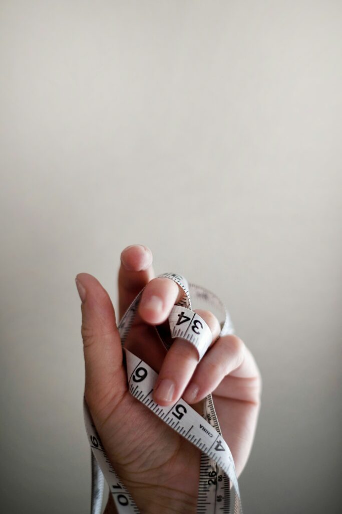En hand håller ett upprullat måttband med synliga siffror, mot en vanlig bakgrund.