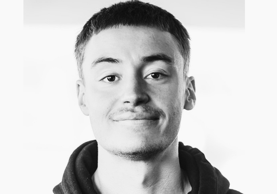 Portrait of a young man with short hair and a subtle smile against a light background (black and white).