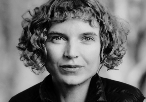 Black-and-white portrait of a woman with short curly hair looking directly at the camera, wearing a dark jacket.