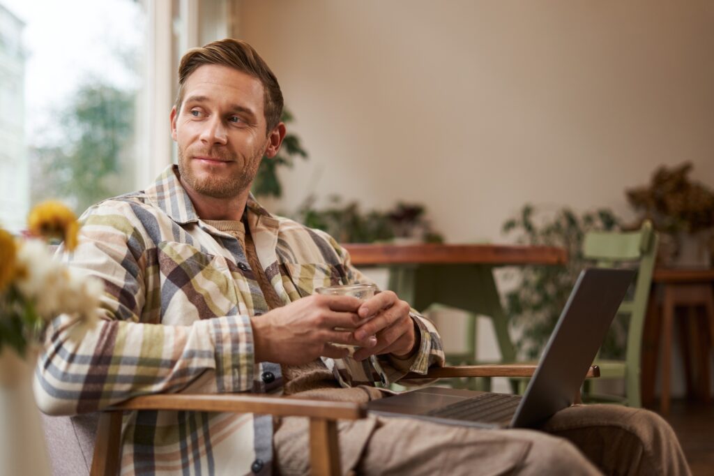 Handsome young professional, businessman sitting in cafe with glass of coffee and working on laptop