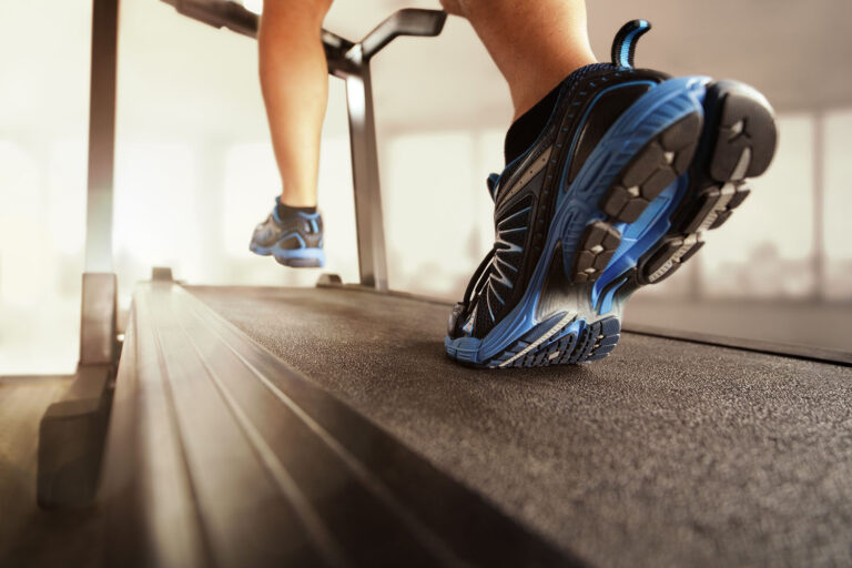 Close-up of blue running shoes on a treadmill belt as someone runs in a gym.