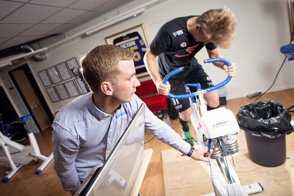 Trainer or technician adjusting a stationary bike for a cyclist in a sports-science lab.