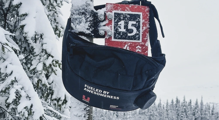 Black crossbody bag in a snowy forest, with a red ski bib marked '15' inside.