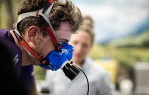 Close-up of a man wearing a blue respirator mask with red-gray straps, concentrating on a task outdoors