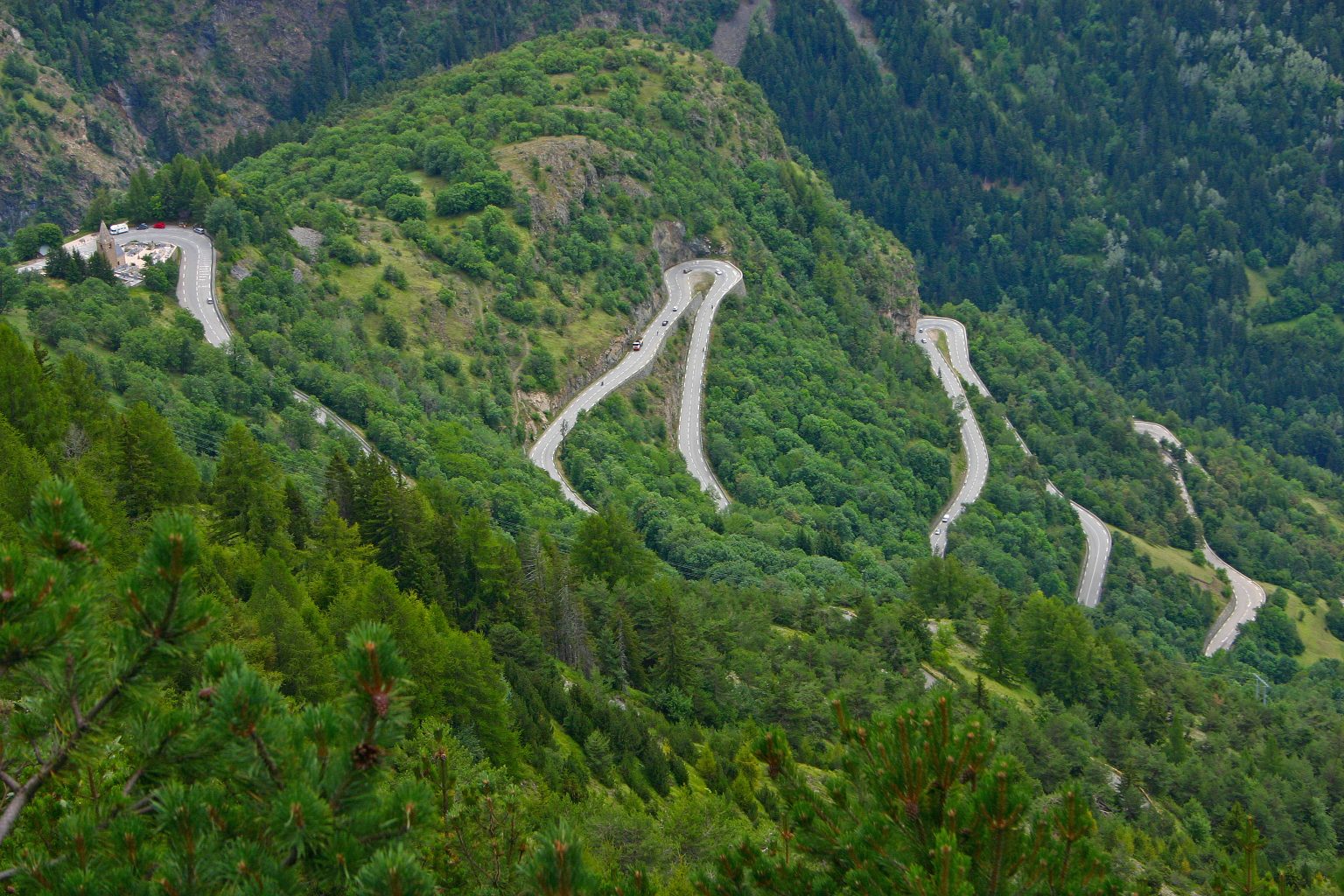 Aerial view of a winding mountain road weaving through a dense green forest and rocky hillsides.