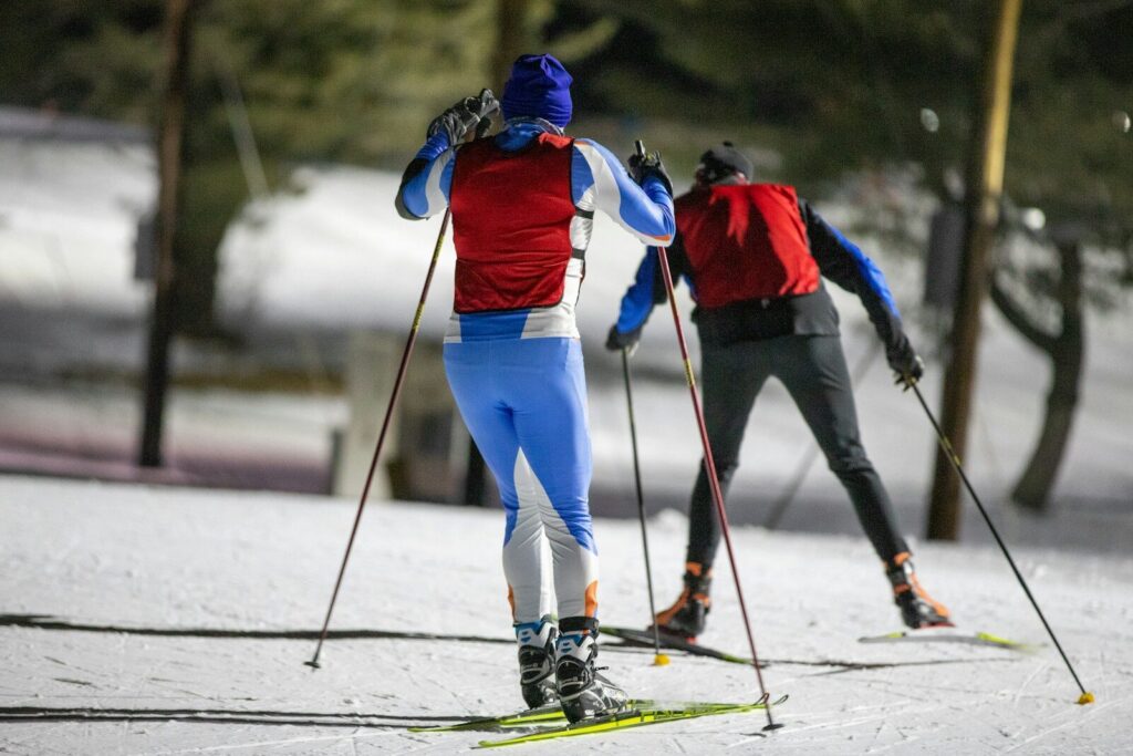 Bild - Aktivitus a couple of people riding skis down a snow covered slope
